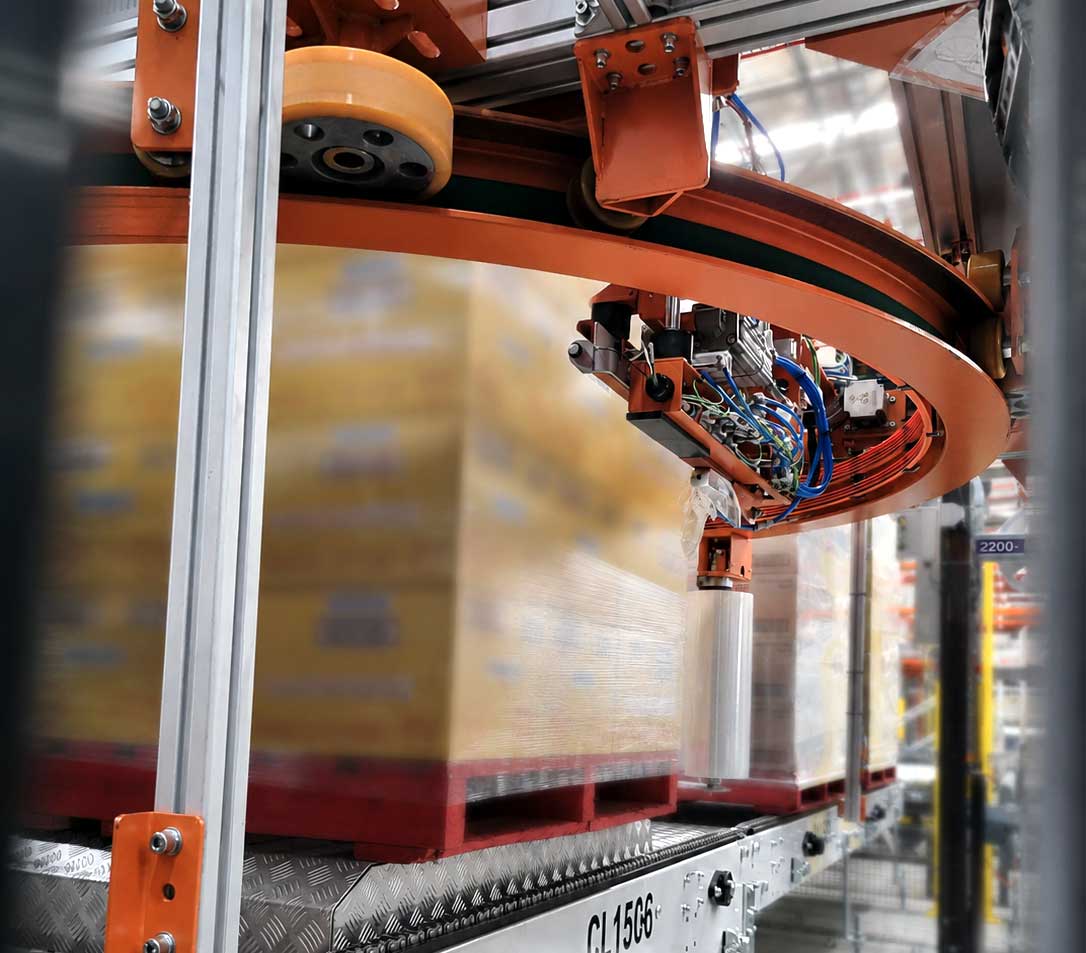 Close-up of the rotary ring and film carriage mid-cycle, applying stretch film to a pallet of cartons